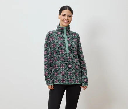 Une femme souriante portant un pull en polaire vert à motifs roses et noirs et un legging noir sur un fond blanc.