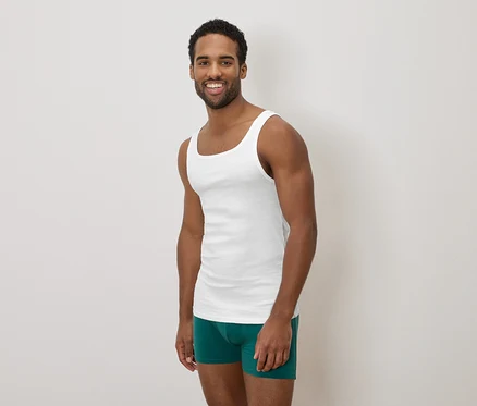 Homme à la peau foncée souriant, portant un débardeur blanc et un caleçon de bain vert.