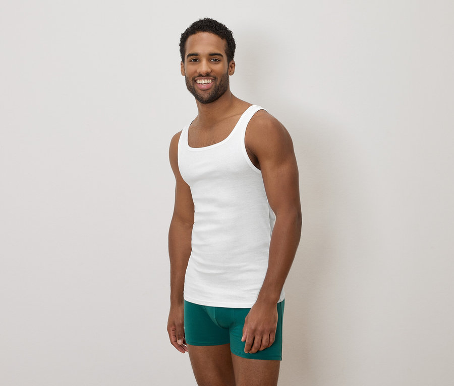 Homme à la peau foncée souriant, portant un débardeur blanc et un caleçon de bain vert.