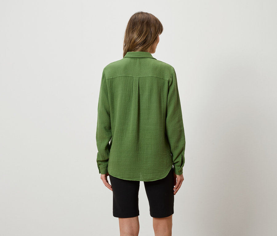 Vue de dos d'une femme aux longs cheveux bruns portant une chemise verte et un short noir sur un fond blanc.