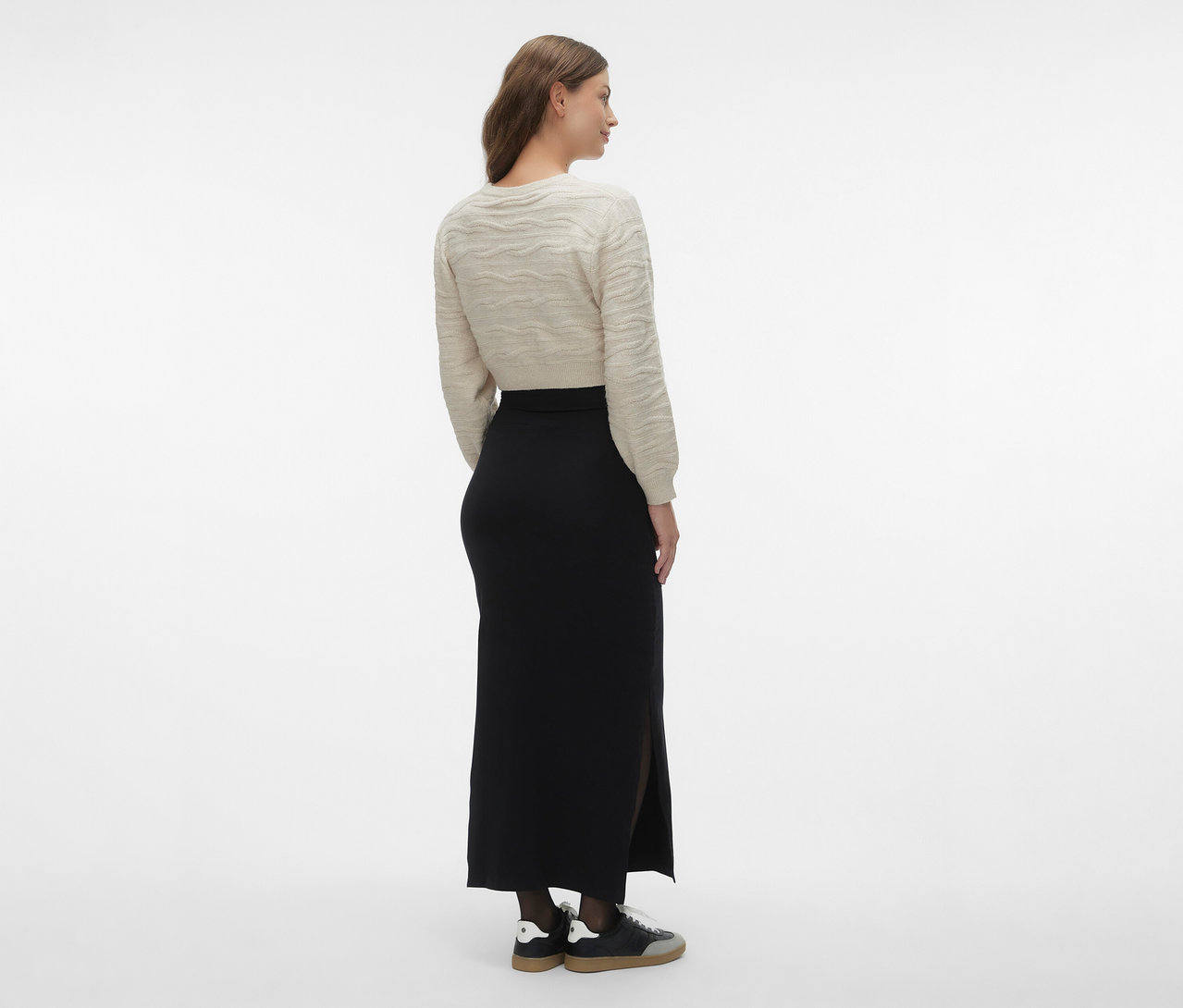 Femme vue de dos portant un pull beige et une jupe maxi noire MAMALICIOUS «	MLEMMA TUBE	» avec fente et des baskets.
