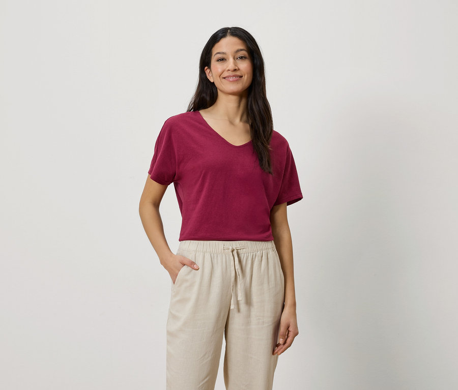 Femme aux cheveux foncés portant un t-shirt bordeaux et un pantalon beige.