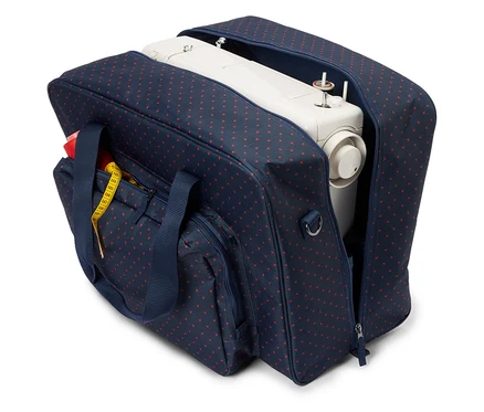 Une machine à coudre blanche dans un sac bleu marine ouvert avec des cœurs rouges. Un ruban à mesurer jaune est attaché à la poche extérieure.