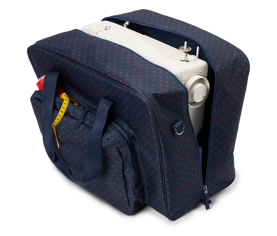 Une machine à coudre blanche dans un sac bleu marine ouvert avec des cœurs rouges. Un ruban à mesurer jaune est attaché à la poche extérieure.