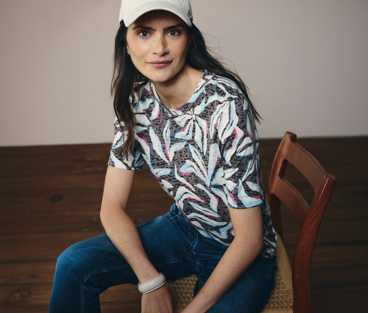 Une femme portant une casquette blanche est assise et porte un t-shirt manches courtes CECIL bleu à motifs.
