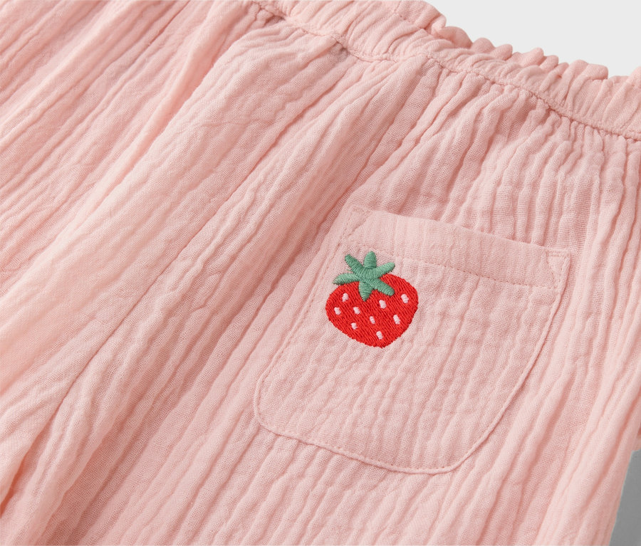 Gros plan sur un short rose avec une broderie de fraise sur la poche.