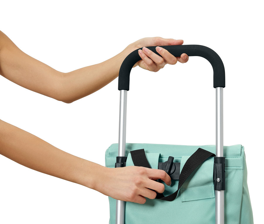 Une personne attache un sac bleu clair avec des sangles noires à un chariot avec des barres argentées et une poignée noire.