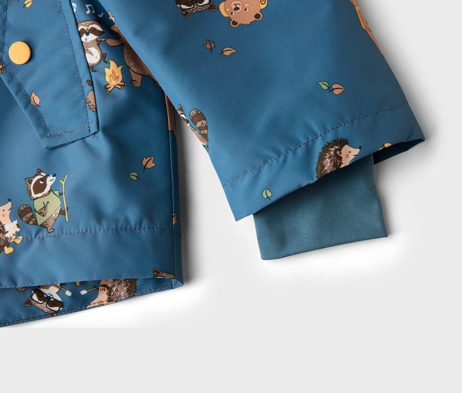 Gros plan sur une veste bleu-vert à motifs d'animaux, notamment des ratons laveurs, des ours et des hérissons, ainsi que des feuilles et des feux de camp.