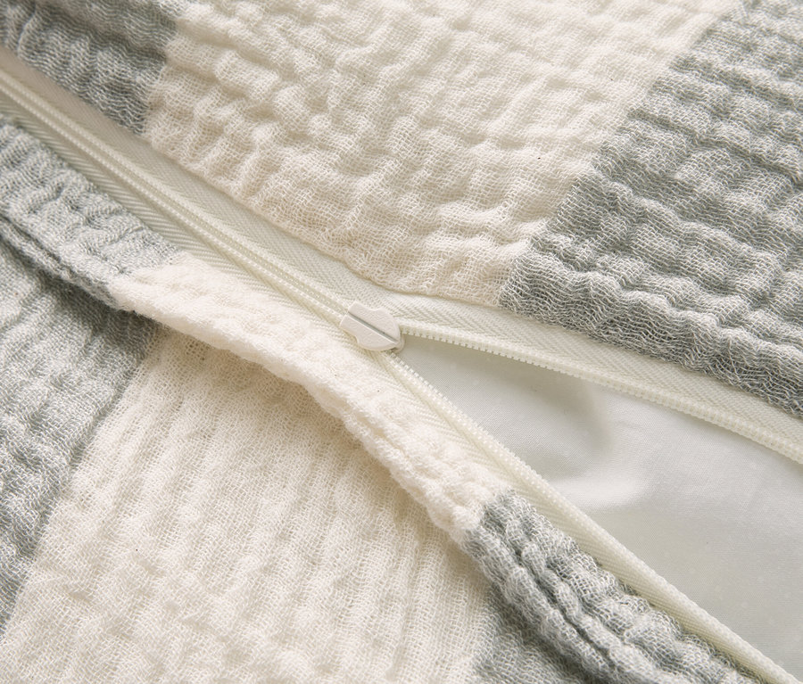 Gros plan d'un coussin à carreaux gris et blancs avec une fermeture éclair blanche partiellement ouverte.