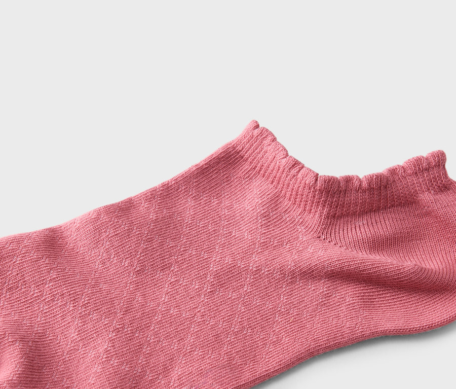 Gros plan d'une seule chaussette rose à bordure à volants sur fond neutre.