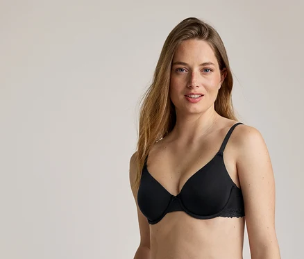 Une femme aux longs cheveux ondulés châtain clair porte un soutien-gorge noir à armatures avec des finitions en dentelle.