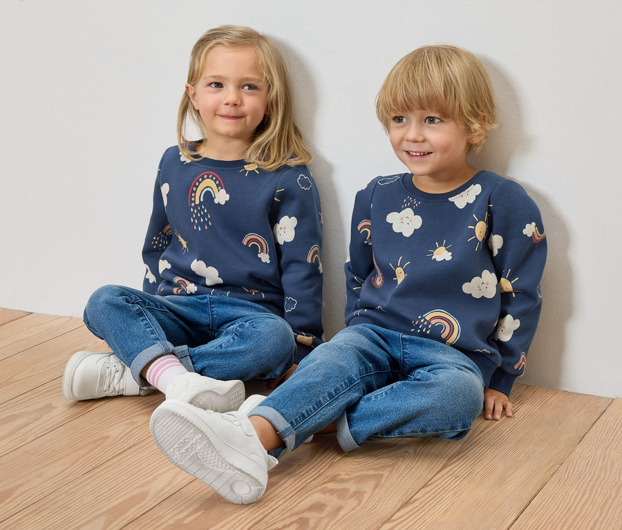 Deux enfants sont assis sur un plancher en bois devant un mur. 