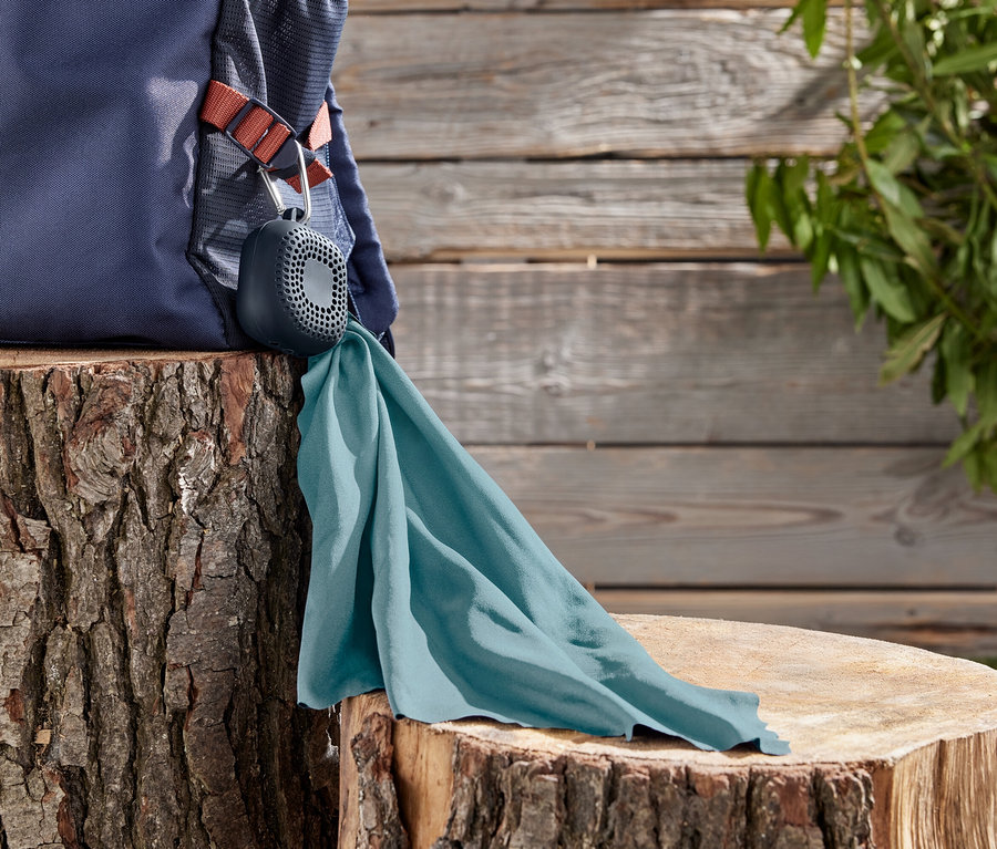Un sac à dos bleu marine repose sur une souche d'arbre, auquel est fixé un haut-parleur gris avec un chiffon turquoise.