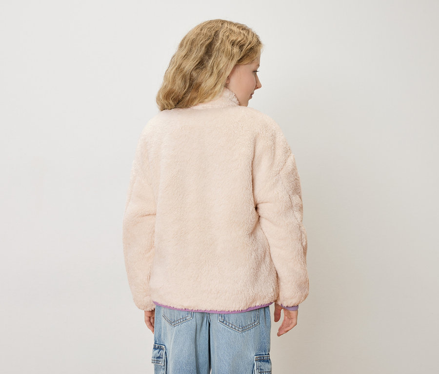 Vue de dos d'une jeune femme aux cheveux blonds ondulés, portant une veste en peluche rose clair et un jean bleu.