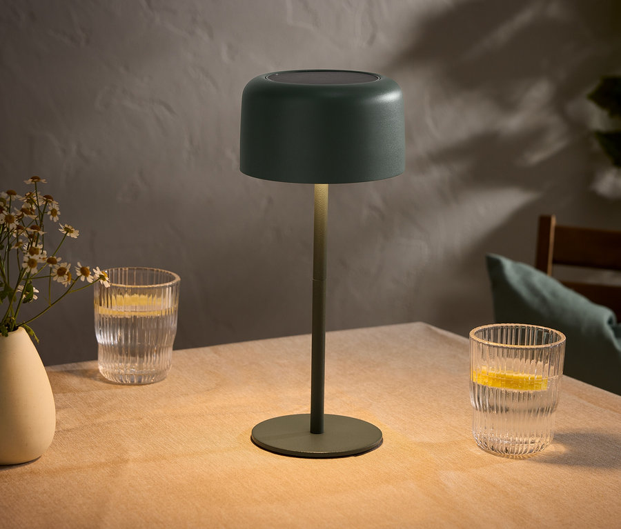 Table avec un vase de fleurs, deux verres avec des citrons et une lampe verte.