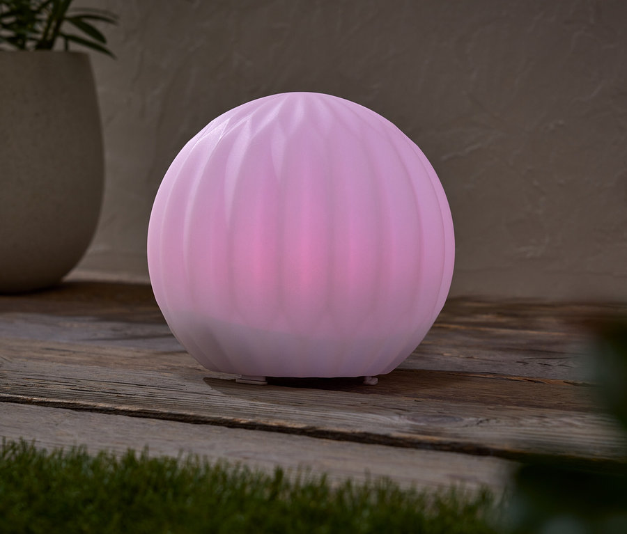 Une lampe sphérique rose est posée sur une table en bois, à côté d'un pot contenant une plante.