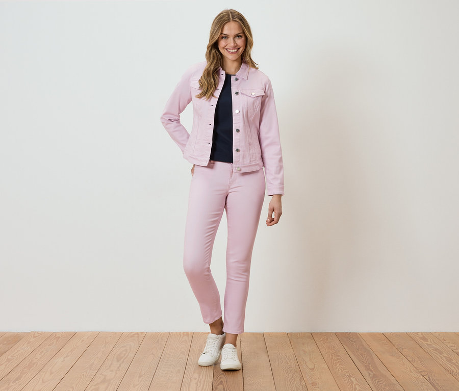 Une femme se tient devant un mur, portant une veste et un pantalon en jean roses.