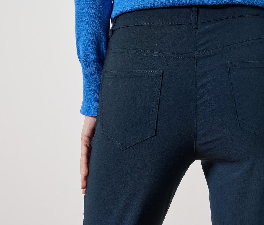 Vue arrière d'une personne portant un pantalon bleu marine et un pull bleu sur un fond clair.
