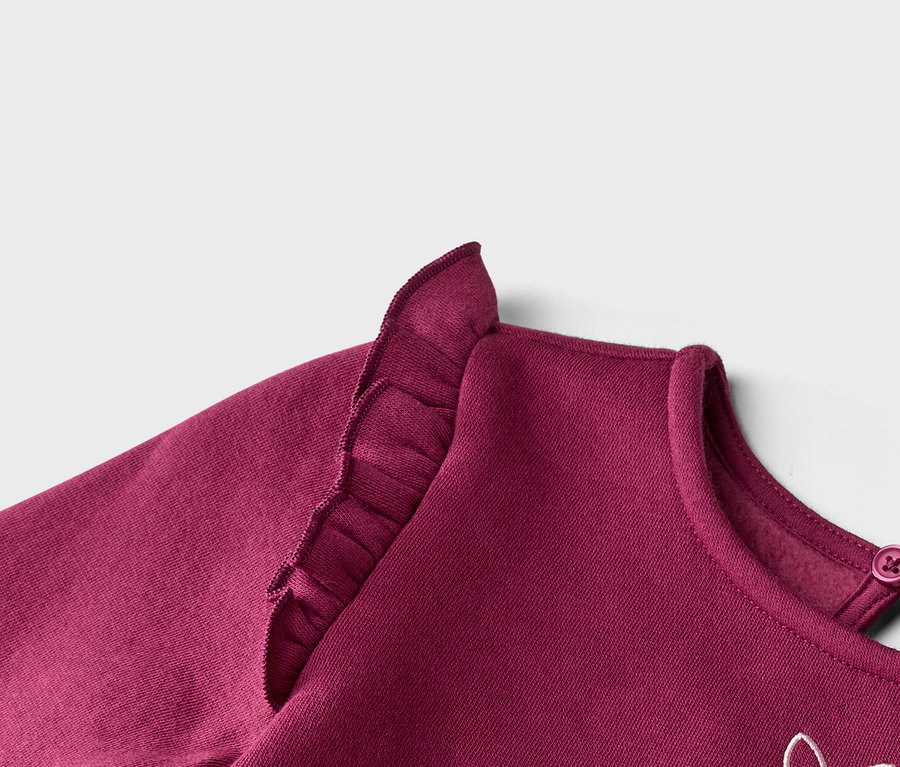 Gros plan sur un sweat-shirt bordeaux avec des volants sur l'épaule et un bouton dans le cou.