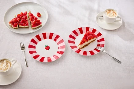Sur une table, des assiettes avec des gâteaux aux fraises, des fourchettes et des tasses avec du latte art.