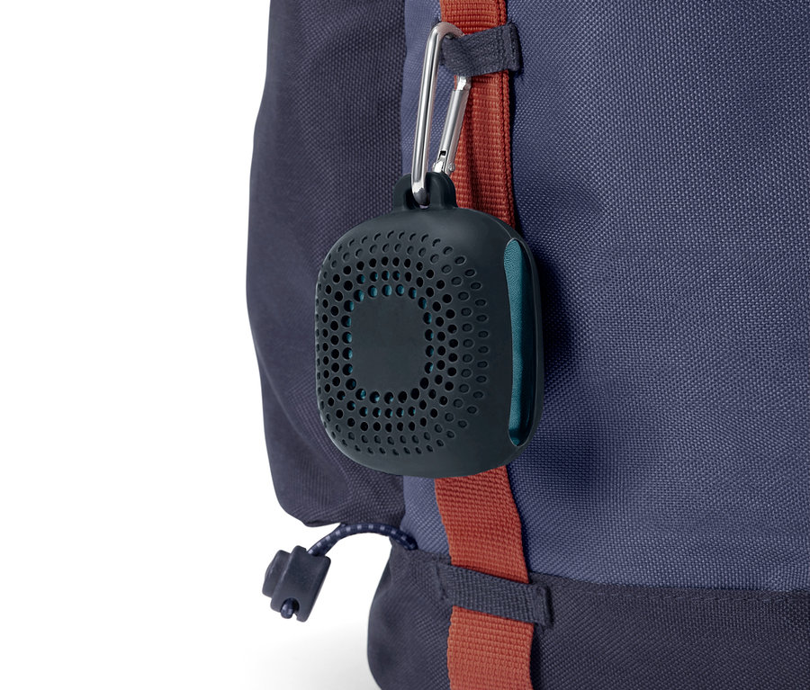 Un étui noir et rond avec des trous est suspendu à un mousqueton sur un sac à dos bleu.