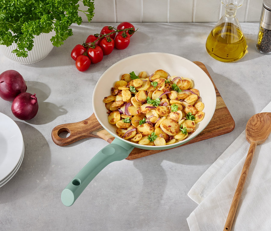 Pommes de terre sautées avec oignons et persil dans une poêle claire sur une table en bois avec accompagnements.