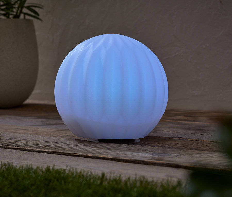 Une lampe sphérique lumineuse est posée sur une table en bois, à côté d'un pot contenant une plante.