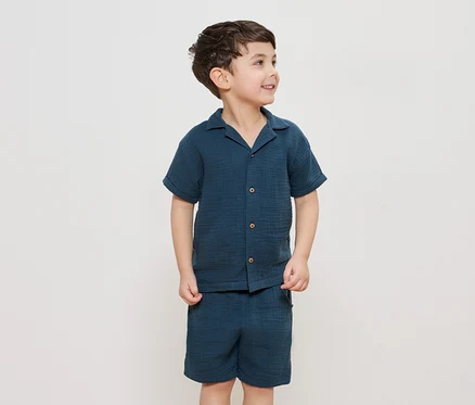 Un garçon porte une chemise boutonnée bleu marine et un short assorti.