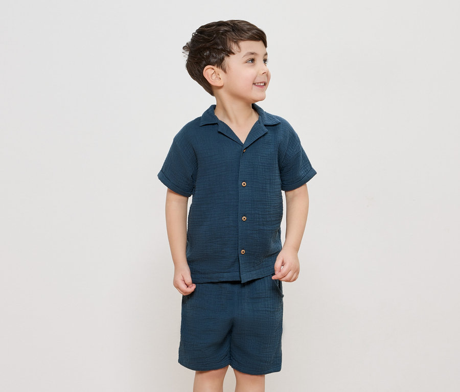 Un garçon porte une chemise boutonnée bleu marine et un short assorti.