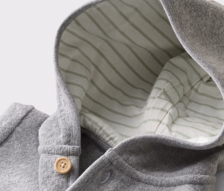 Gros plan d'un manteau à capuche gris avec un bouton en bois et une doublure rayée.