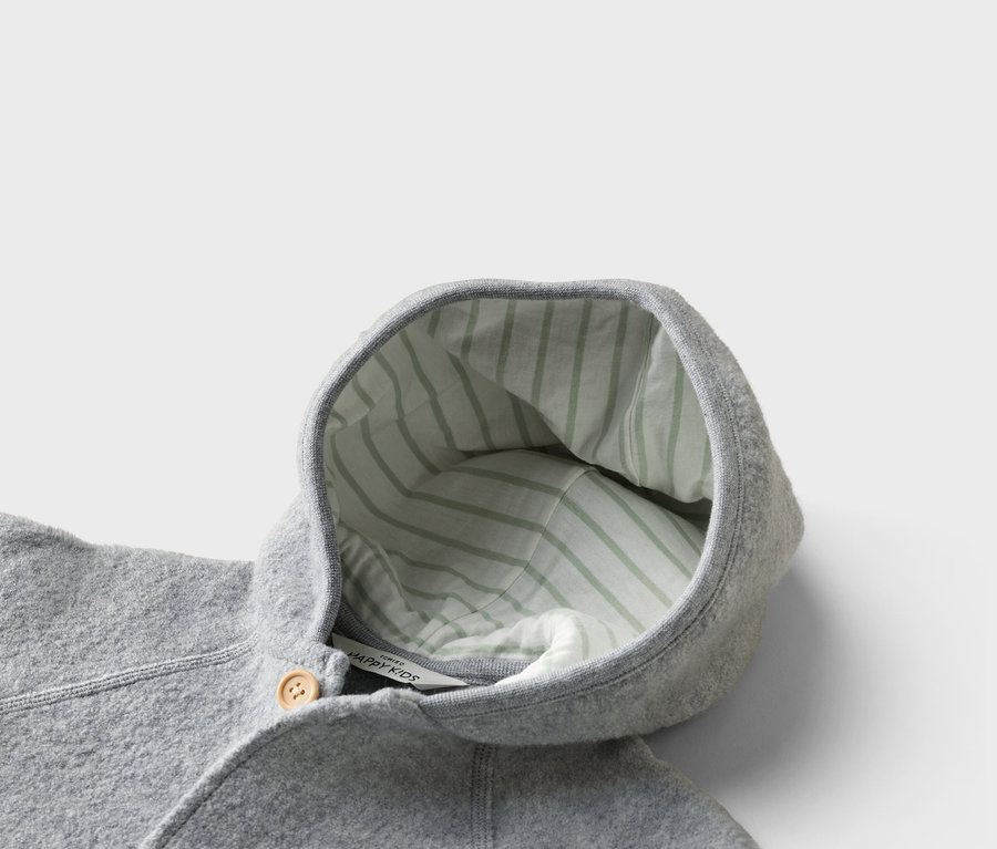 Gros plan sur une veste grise pour enfant avec une capuche doublée d'un tissu rayé vert clair et un bouton en bois.