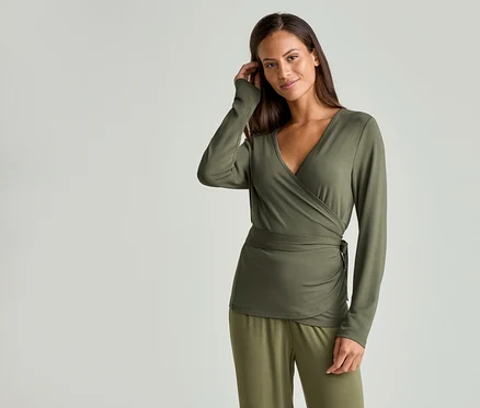 Une femme portant un haut cache-cœur vert olive à manches longues et un pantalon assorti se touche les cheveux.