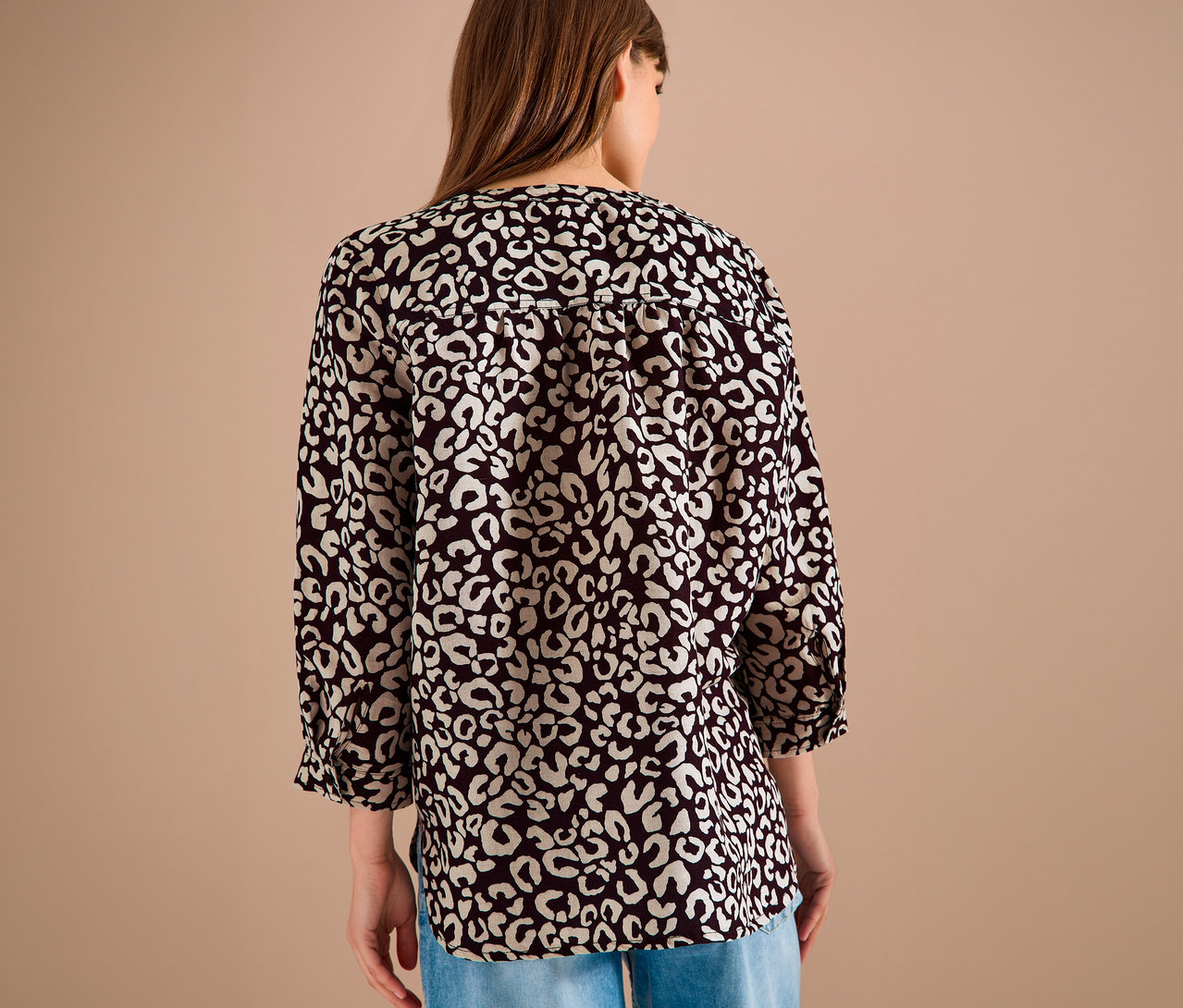 Vue arrière d'une femme aux cheveux bruns portant un chemisier à motifs noirs et blancs et un jean.