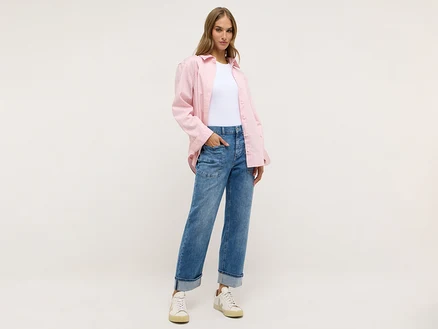 Une femme porte un pantalon clair, un t-shirt blanc et une chemise rose.