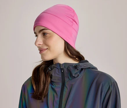 Femme aux cheveux bruns portant un bonnet rose et une veste réfléchissante foncée, regardant vers la droite et souriant légèrement.