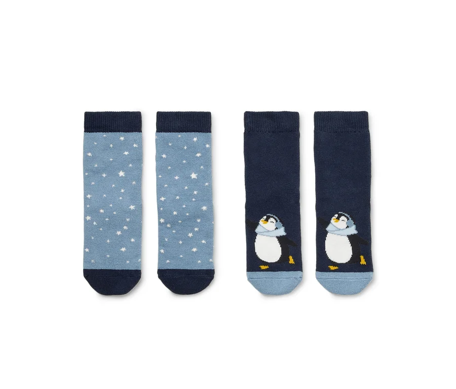 Deux paires de chaussettes posées côte à côte. À gauche, une paire bleu clair à étoiles blanches, à droite, une paire bleu foncé avec un motif de pingouin. Les deux paires ont des bords-côtes et des pointes bleu foncé.