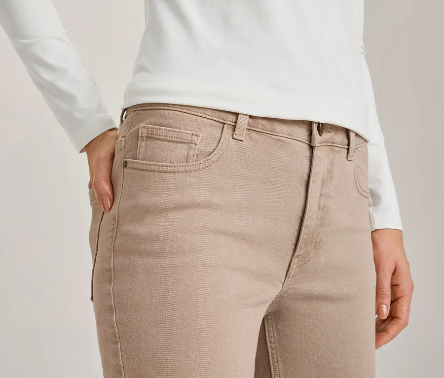 Gros plan d'une personne portant un haut blanc à manches longues et un jean marron clair, une main dans la poche avant.