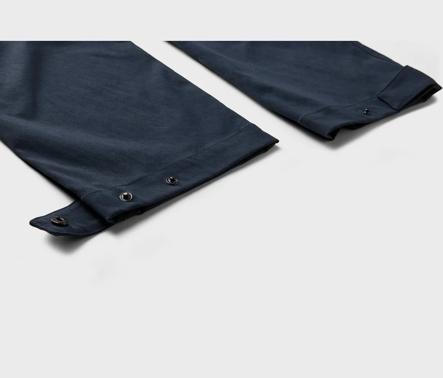 Gros plan sur deux jambes de pantalon bleu marine sur fond blanc. La jambe gauche a une sangle déboutonnée avec un bouton-pression, révélant un autre bouton-pression sur l'ourlet. La jambe droite est légèrement retroussée.