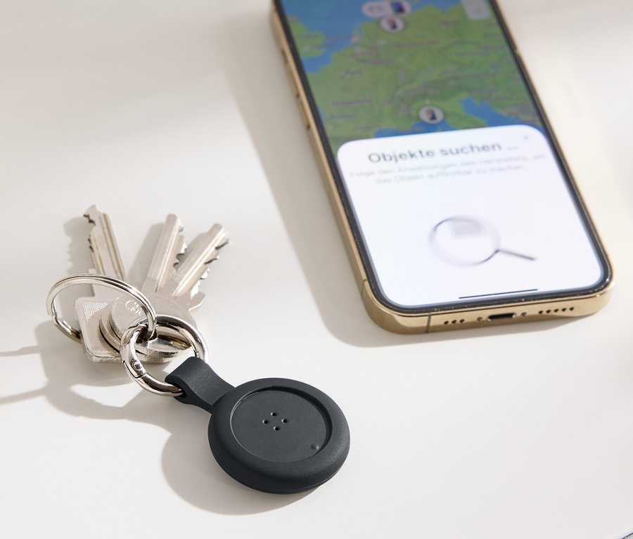 Des clés avec un traceur noir et un téléphone portable avec une carte sur l'écran sont posés sur une table.