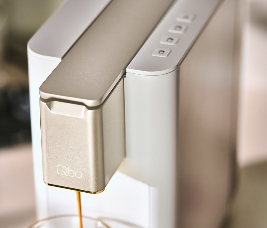 Une machine à café Qbo ICONIC Light Gold verse du café dans une tasse.
