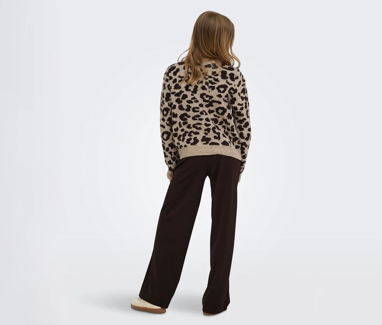 Personne de dos, portant un pull beige à imprimé léopard et un pantalon large marron foncé.
