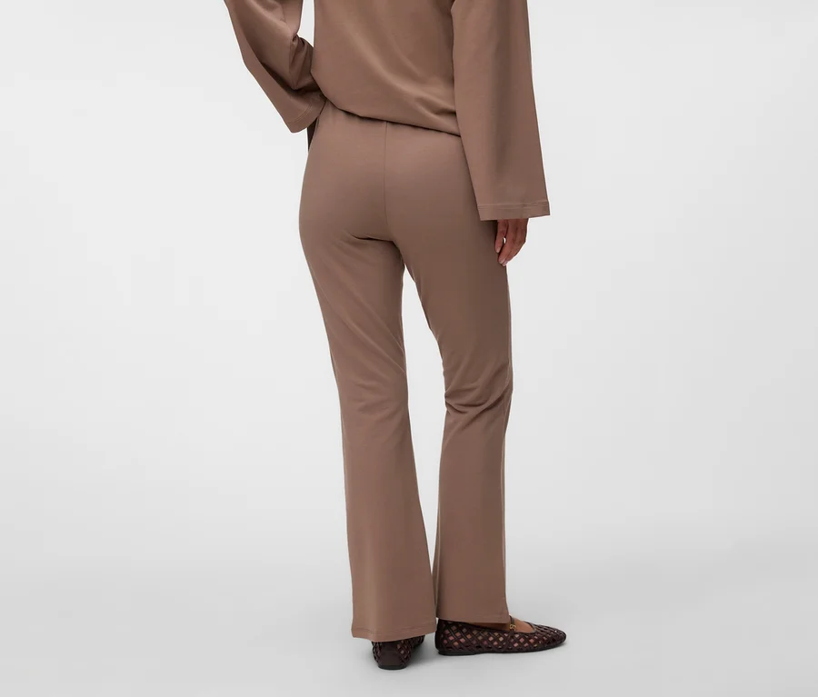 Personne de dos portant un haut marron à manches longues et un pantalon de survêtement évasé marron MAMALICIOUS « MLSINE HW », avec des chaussures plates tressées marron foncé.