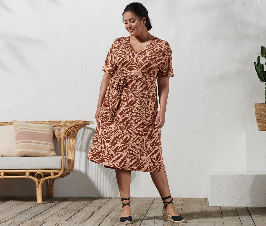 Une femme debout porte une robe en jersey imprimée et des espadrilles à talon compensé.