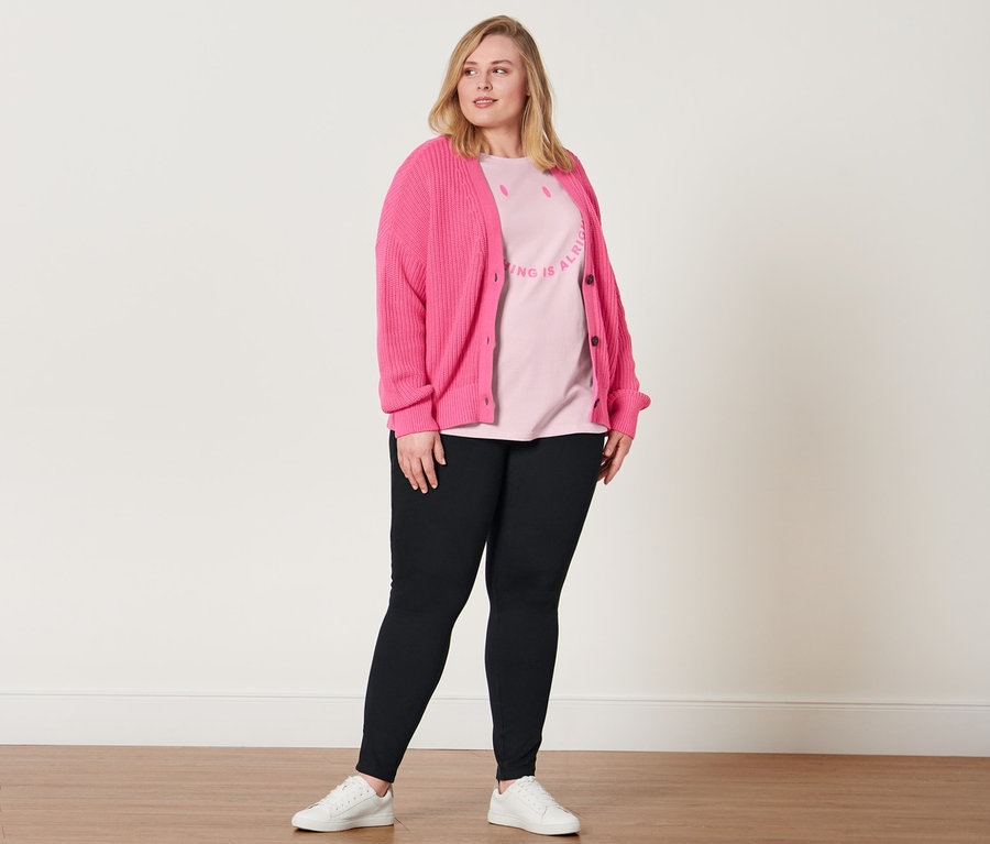 Femme posant en jegging, t-shirt avec inscription imprimée, baskets en cuir et cardigan en grosse maille.