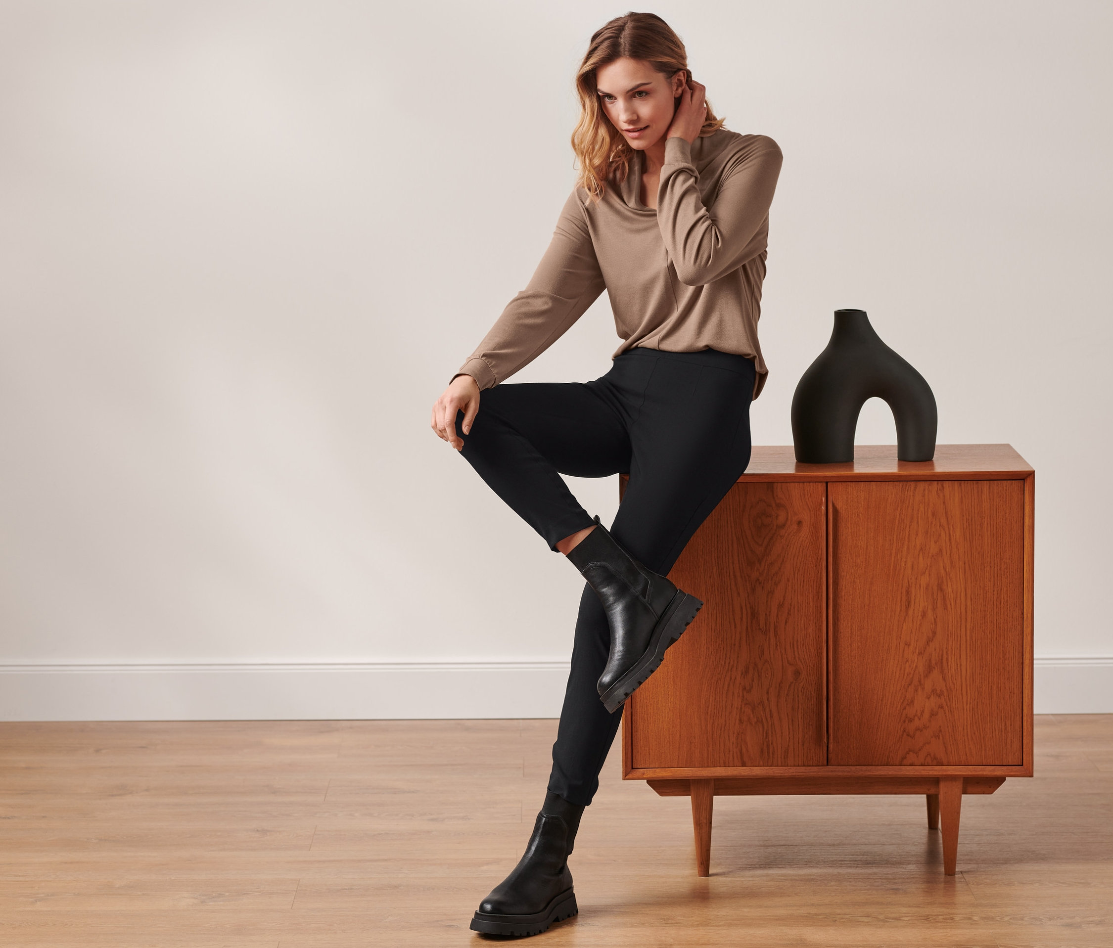 Femme assise sur une armoire portant un pantalon stretch, noir.