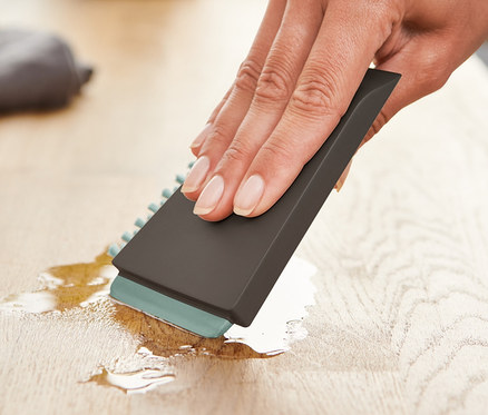 Une femme essuie un liquide sur une surface en bois avec une brosse de cuisine universelle.