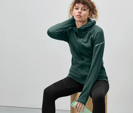 Femme assise sur un bloc de bois, portant une veste thermique vert foncé.