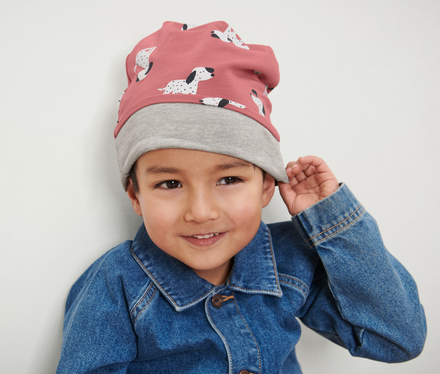 Un garçon porte un bonnet pour enfant rose et gris et une veste en jean.