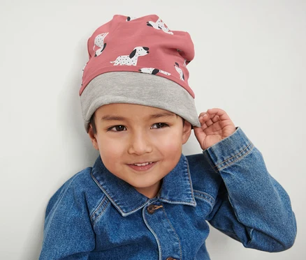 Un garçon porte un bonnet pour enfant rose et gris et une veste en jean.