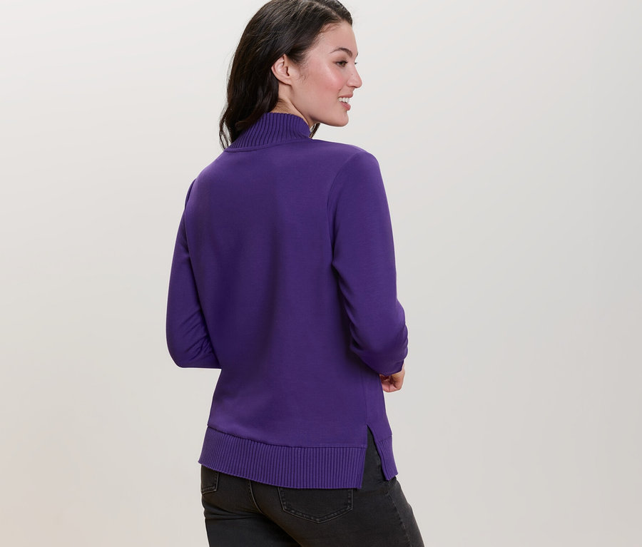 Femme regardant par-dessus son épaule portant un sweatshirt violet avec col montant.